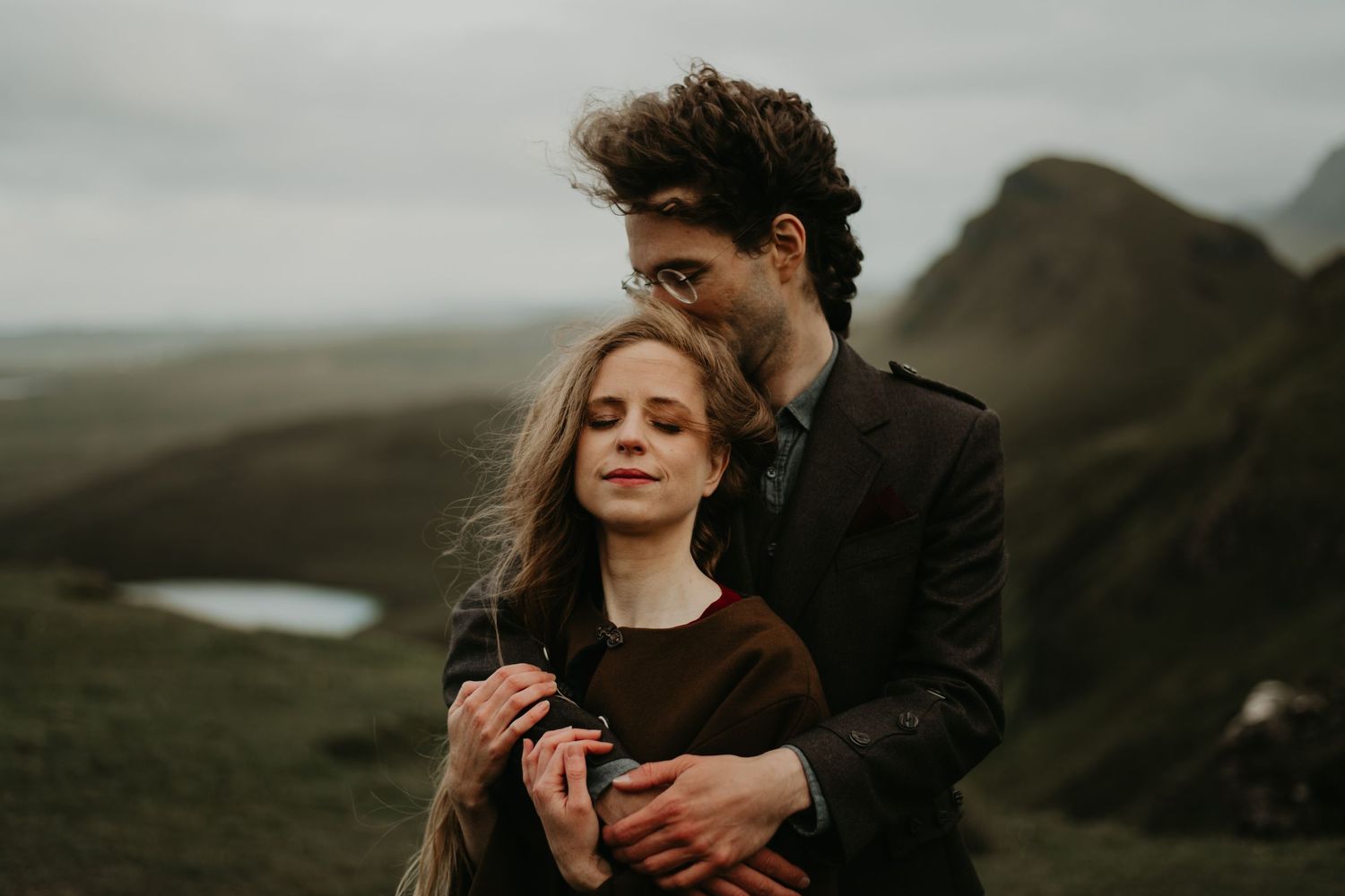 Atmospheric couple's portrait with moody mountains and dramatic skies in background in Isle of Skye Scotland.