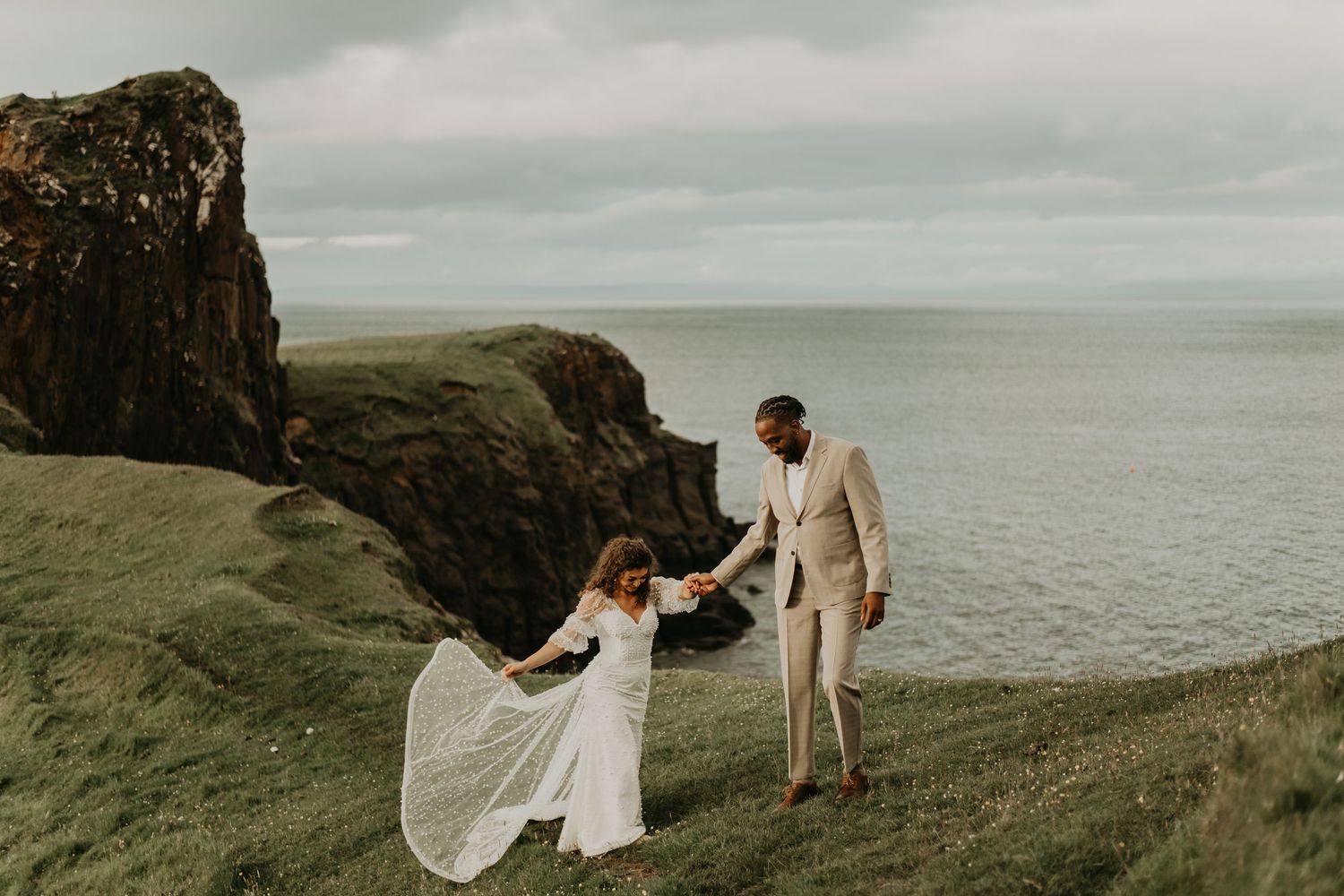 Scenic coastal cliffside engagement photo session with couple along dramatic ocean views and overcast skies.
