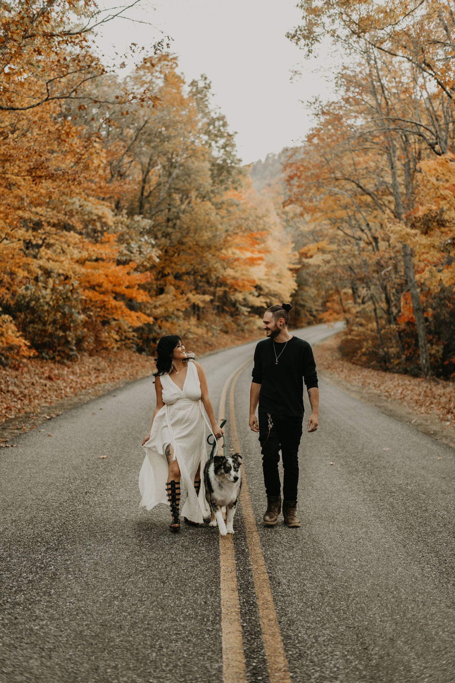 A couple walks down a gravel path surrounded by autumn trees with golden leaves on a romantic fall day.