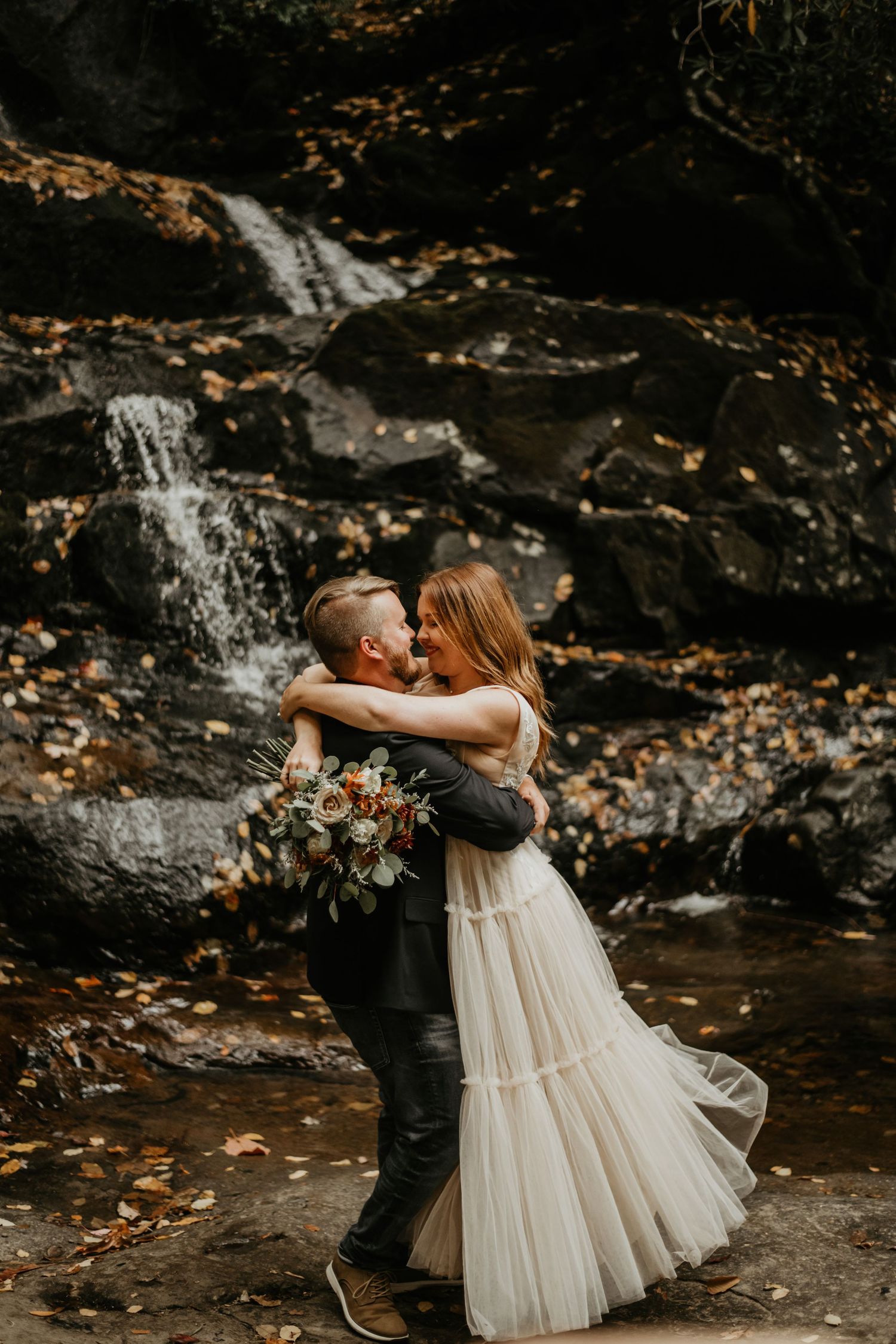 Romantic waterfall wedding photography with couple embracing near cascading water.