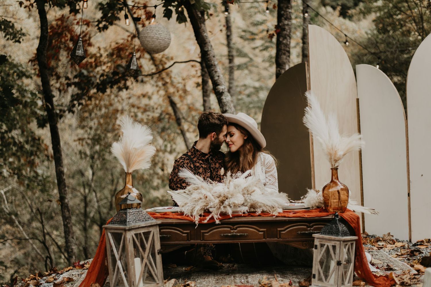 Romantic boho wedding setup with vintage furniture and arched backdrop in forest setting.