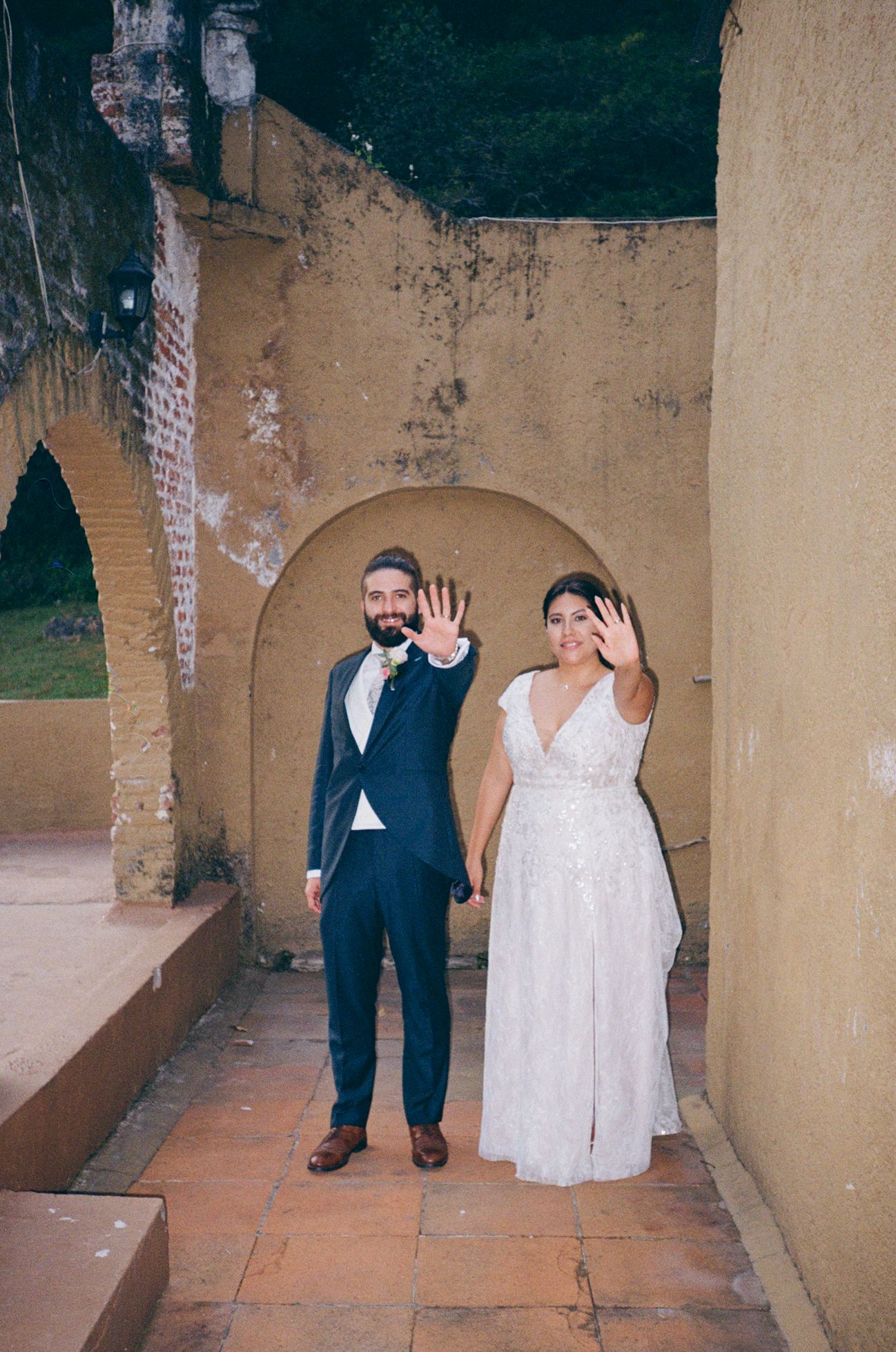 A couple walks along an outdoor corridor with beige stone walls and arched architectural details.