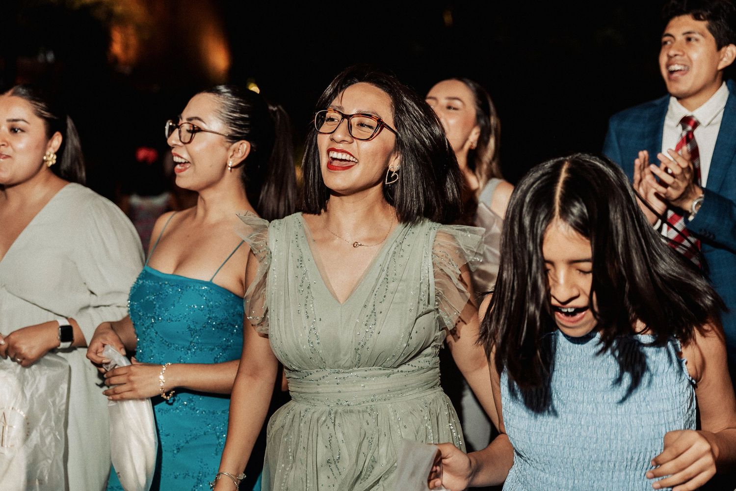 Wedding guests dancing and celebrating together under warm reception lighting.