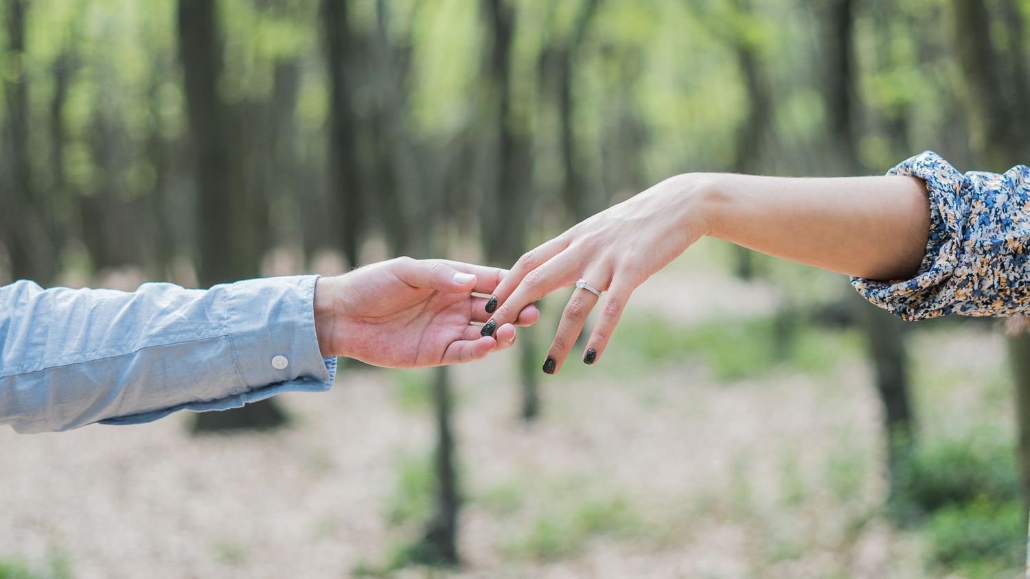 Two hands reaching towards each other against a blurred forest background in romantic gesture.