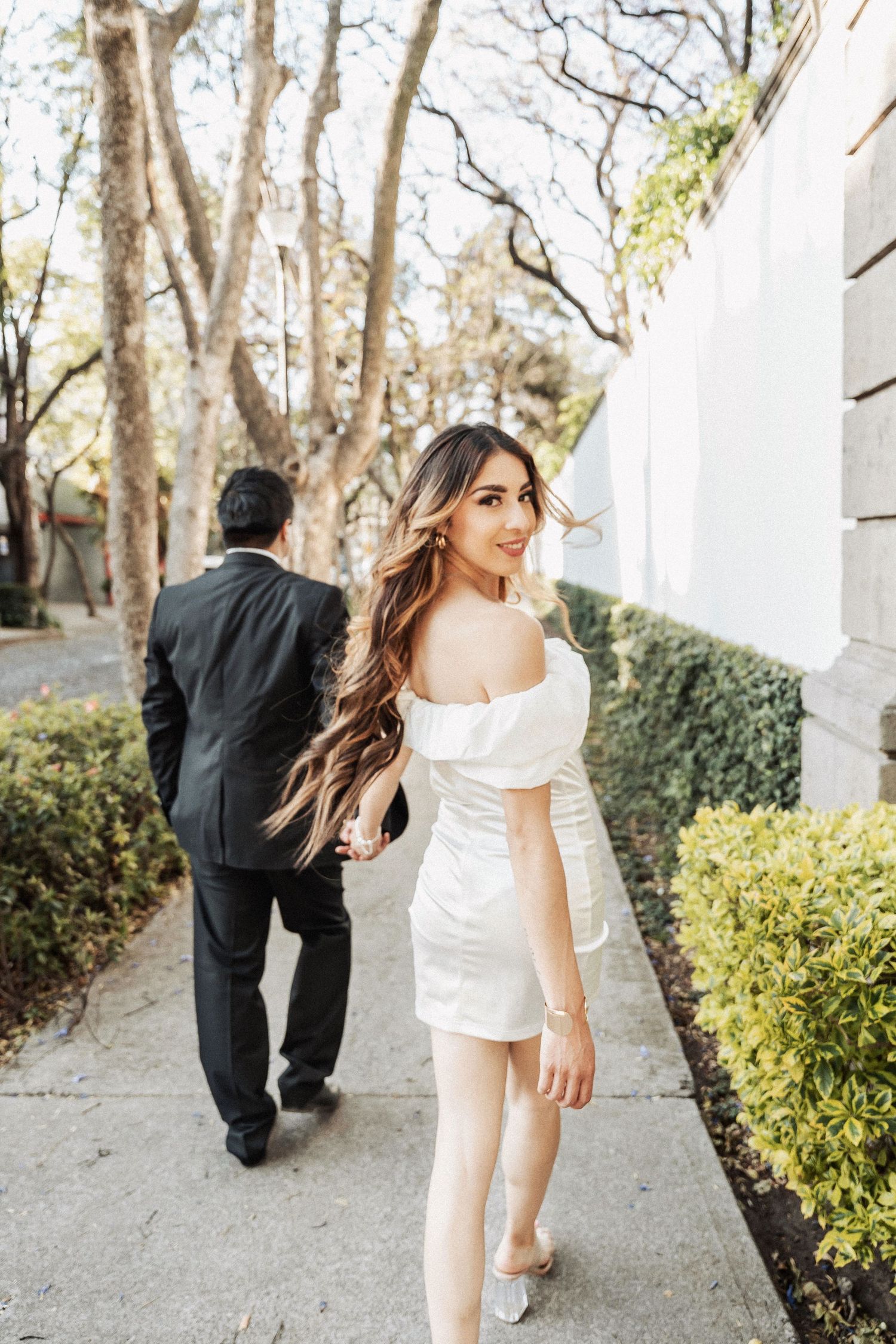 Creative sequence photo showing couple walking and turning away on sidewalk with greenery and trees in background.