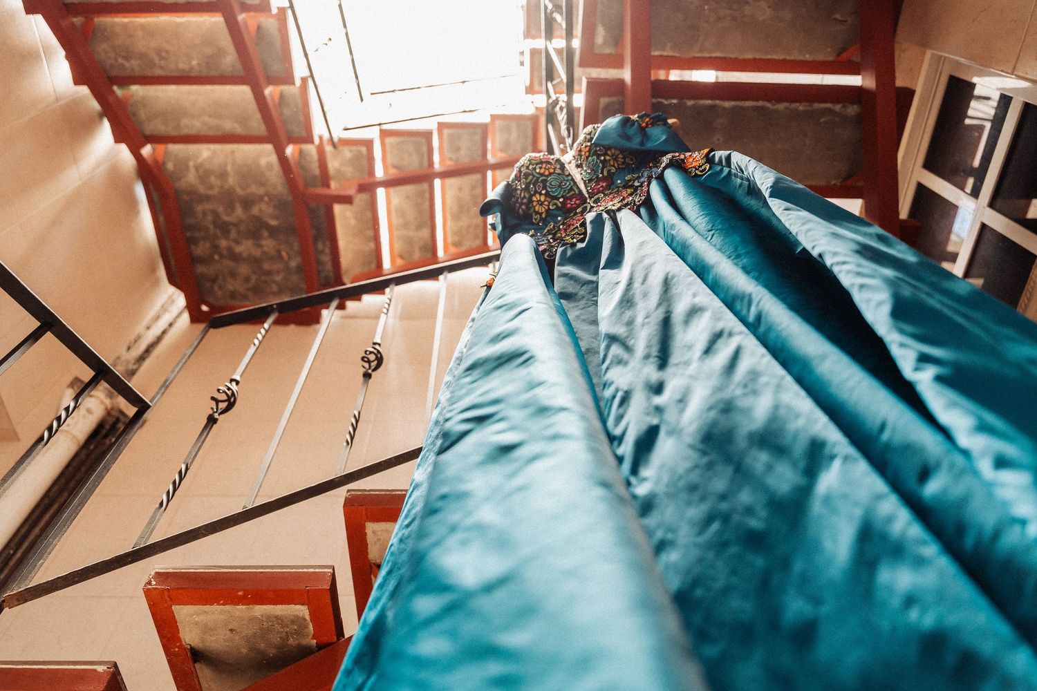 Looking up at turquoise bridesmaid dresses hanging on wooden hangers in a stairwell with natural light.