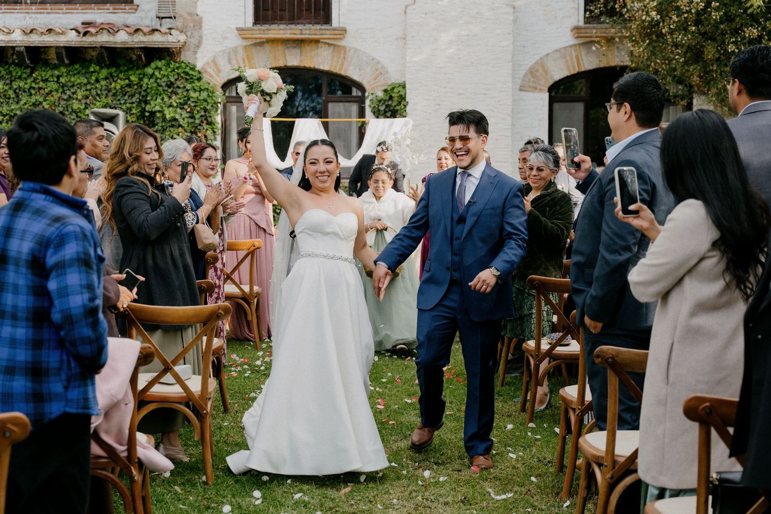 Wedding guests celebrate and dance together during an outdoor garden reception at dusk.
