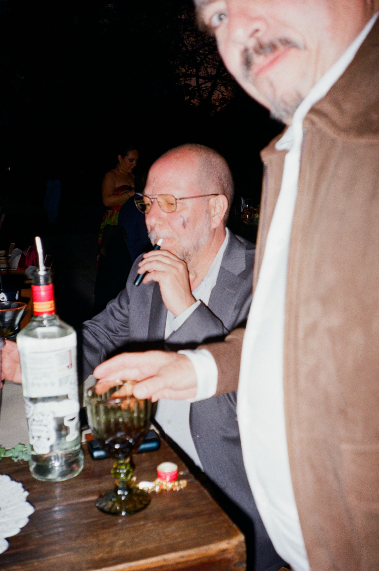 People gathered at a table with drinks and snacks at a dimly lit social gathering.