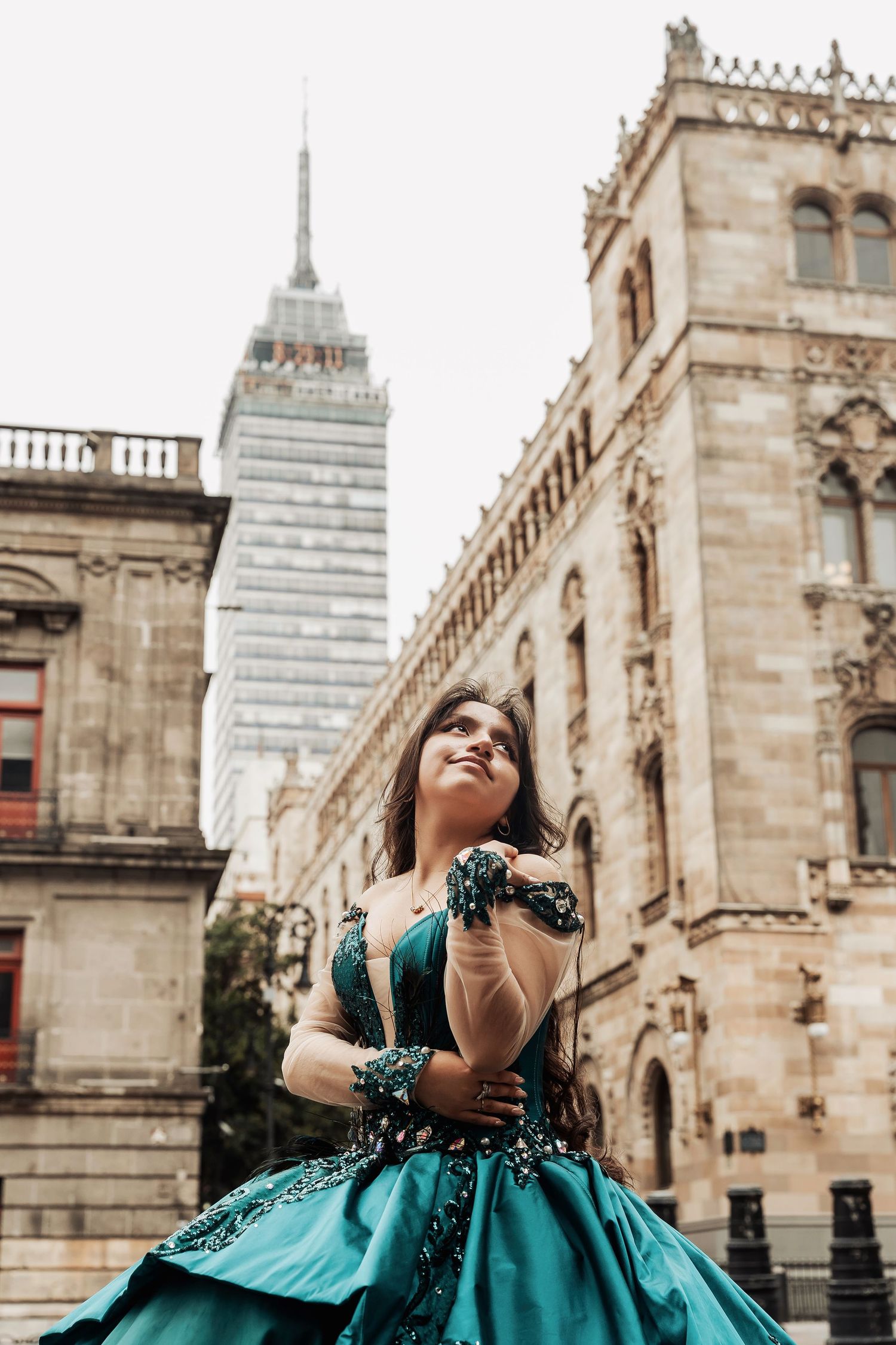 Woman in emerald green gown spins joyfully in front of historic European stone architecture.