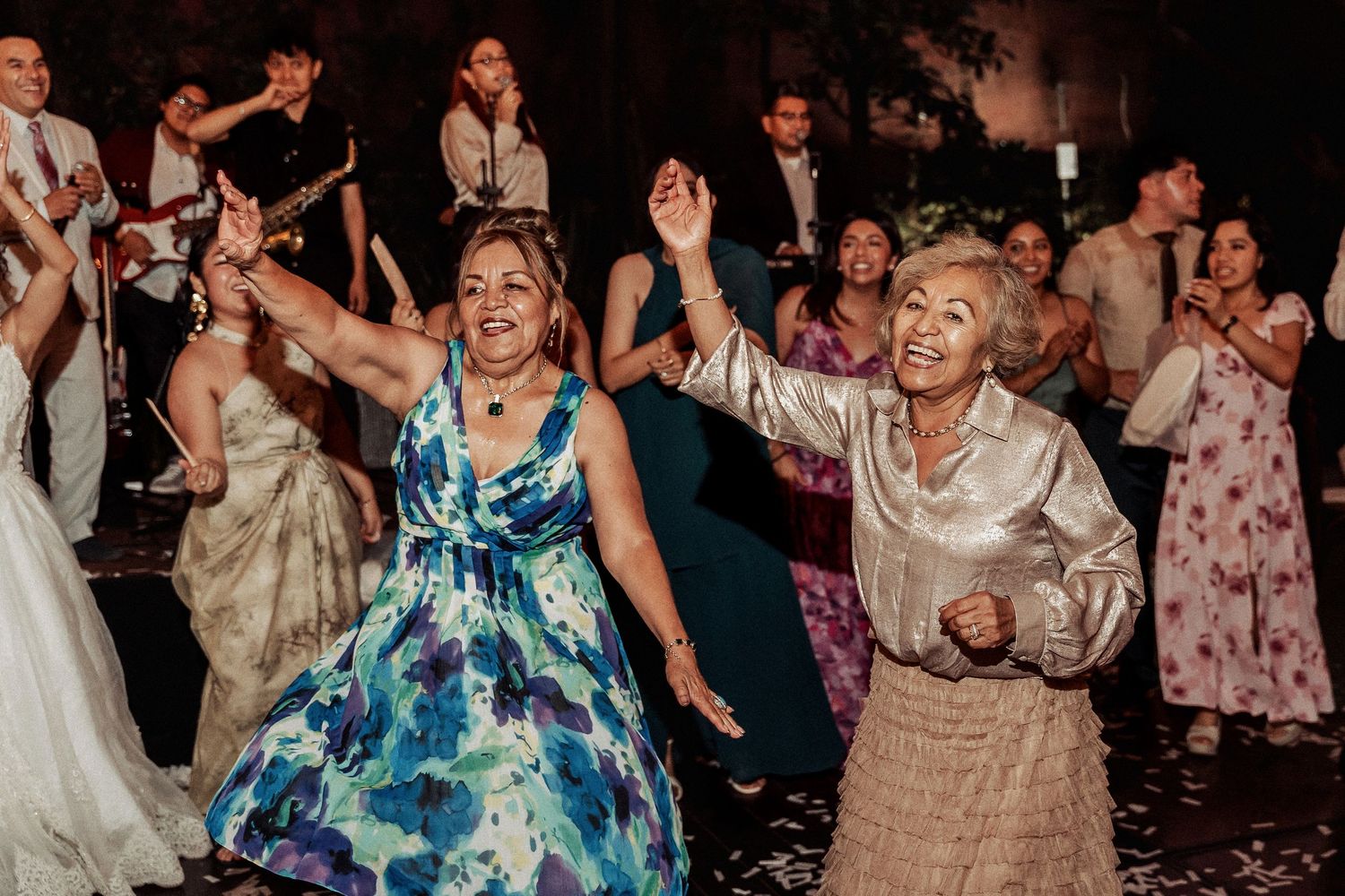 Wedding guests dancing energetically on dimly lit dance floor during reception celebration.