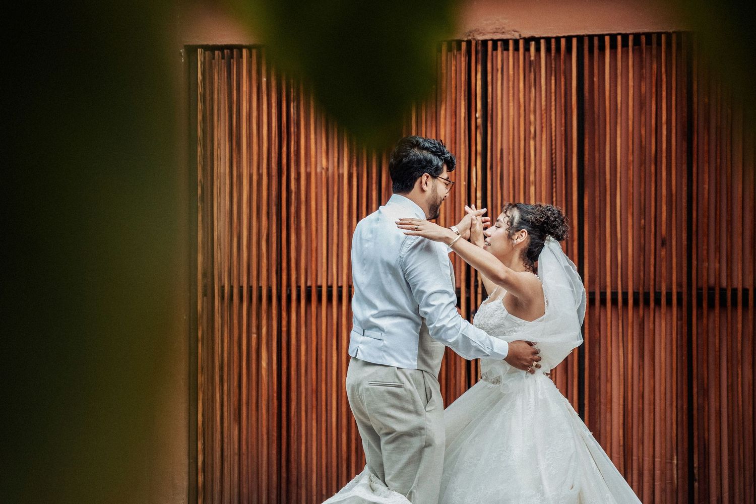 A couple in wedding attire posing against a wooden panel backdrop.