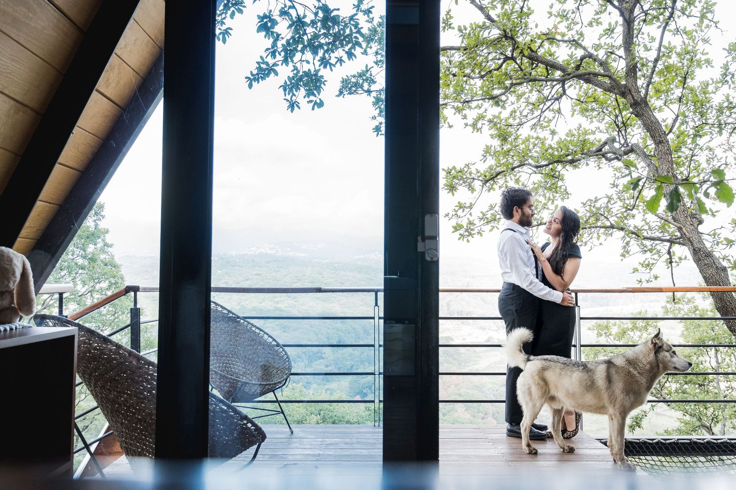 A couple shares a moment on a balcony overlooking mountains with their dog nearby.