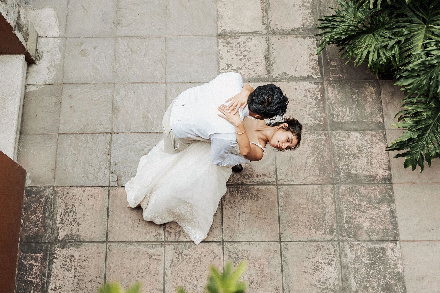Aerial view of couple in white embracing on stone patio.