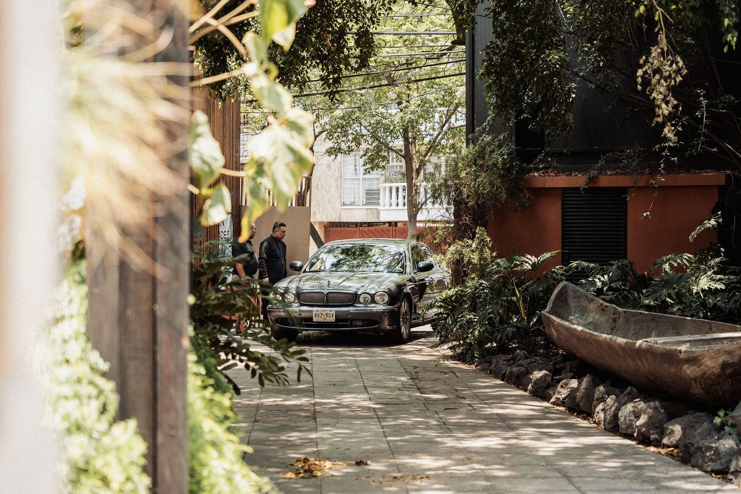 Sun-dappled stone pathway lined with tropical plants and flowers leads through a peaceful garden setting.
