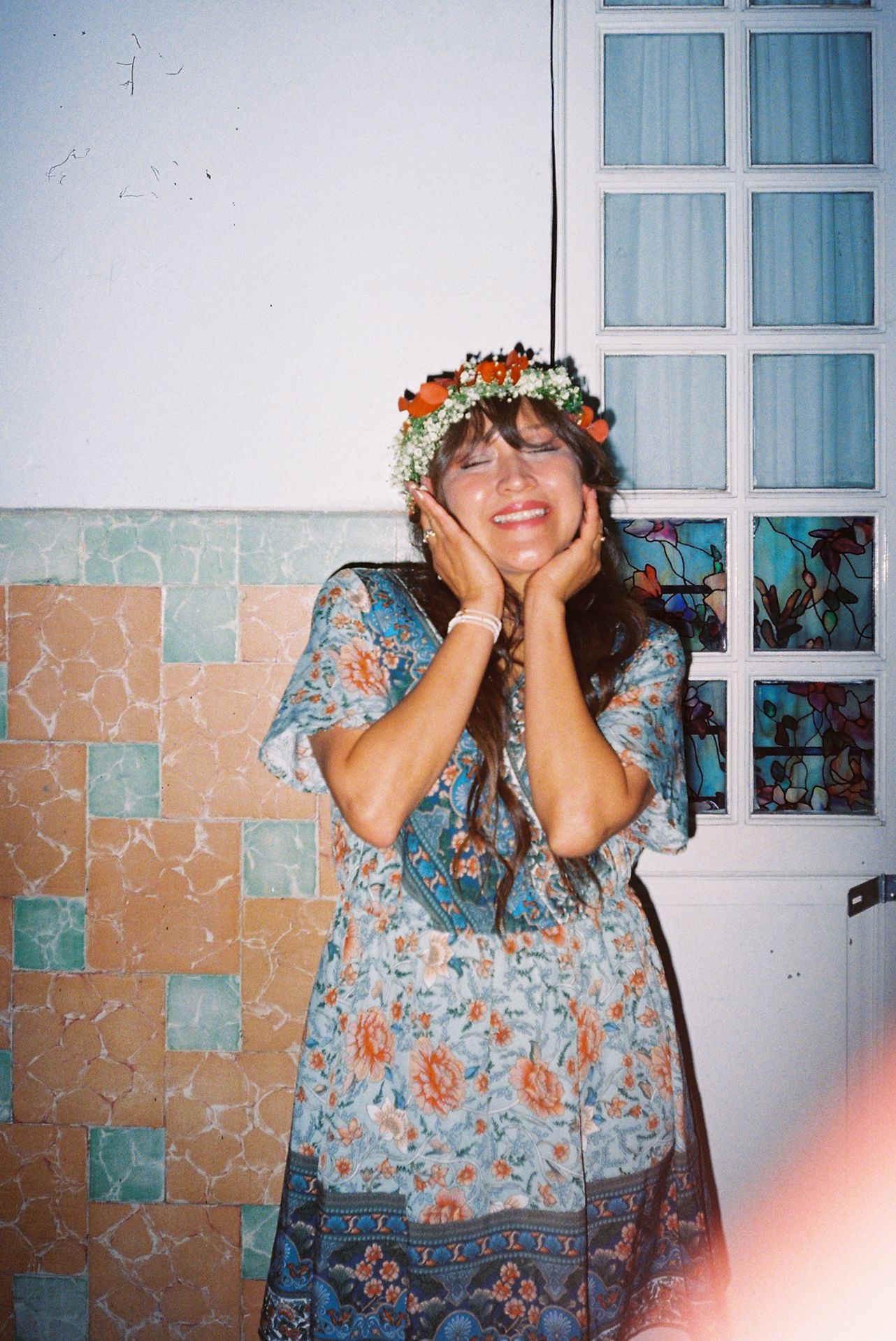 A series of four photos showing someone in a blue floral dress posing playfully against a wall with white windows.