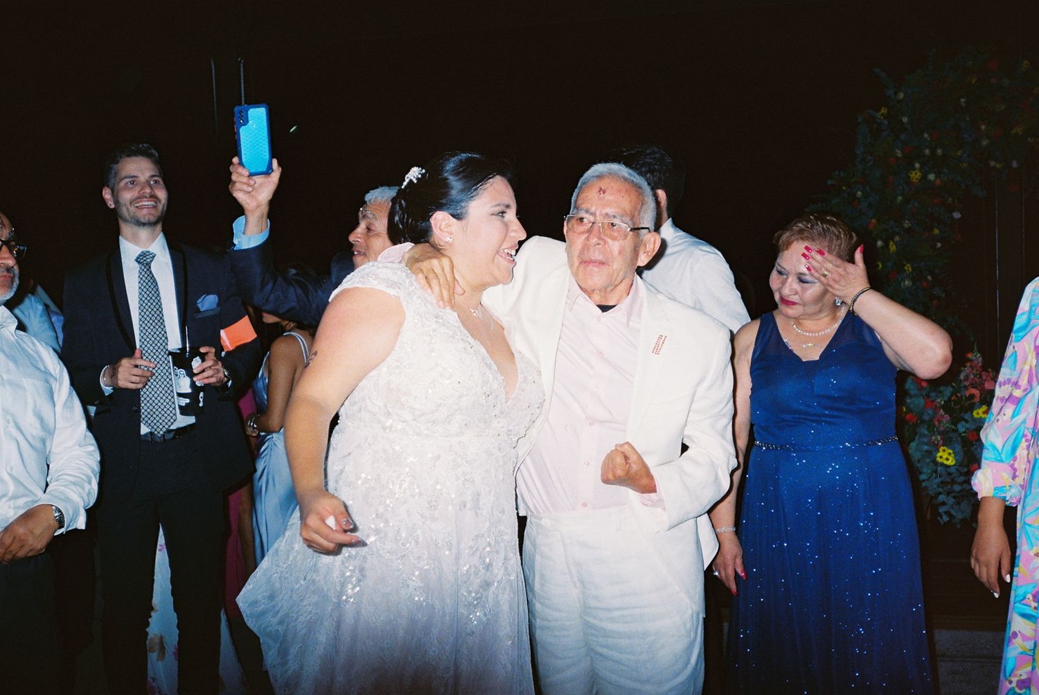 A group of people dancing and celebrating at what appears to be a wedding reception or party.