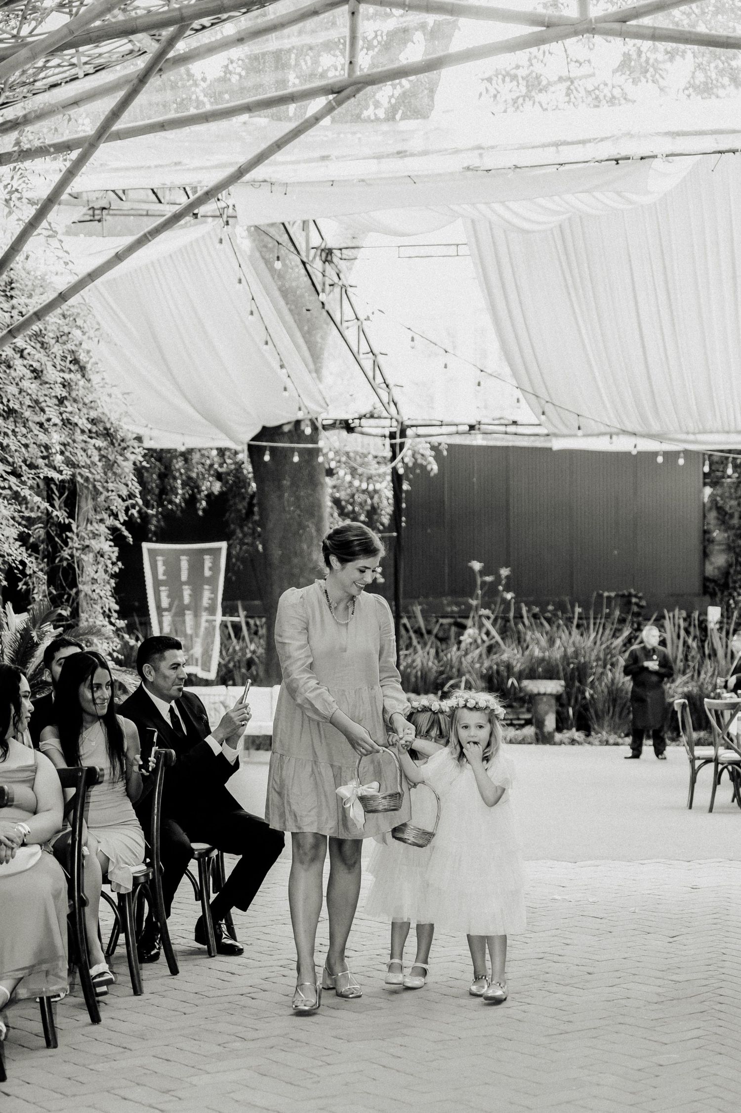 A black and white photograph of guests gathering under a large outdoor tent at a wedding reception.