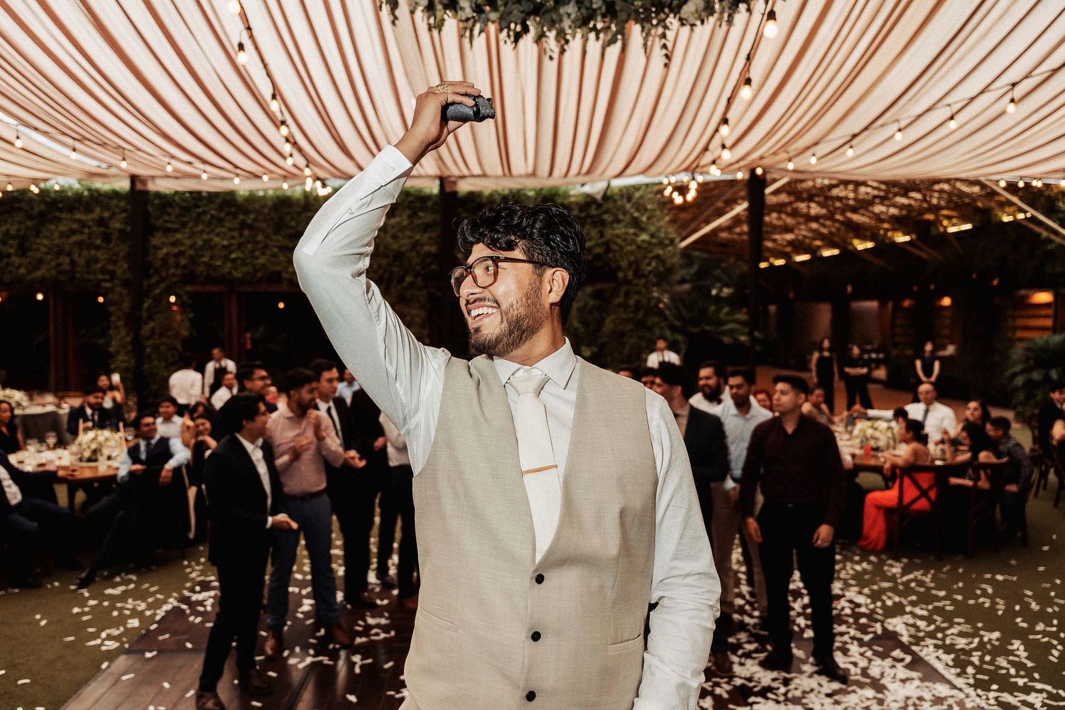 Person in light colored suit raising a glass in celebration at wedding reception.