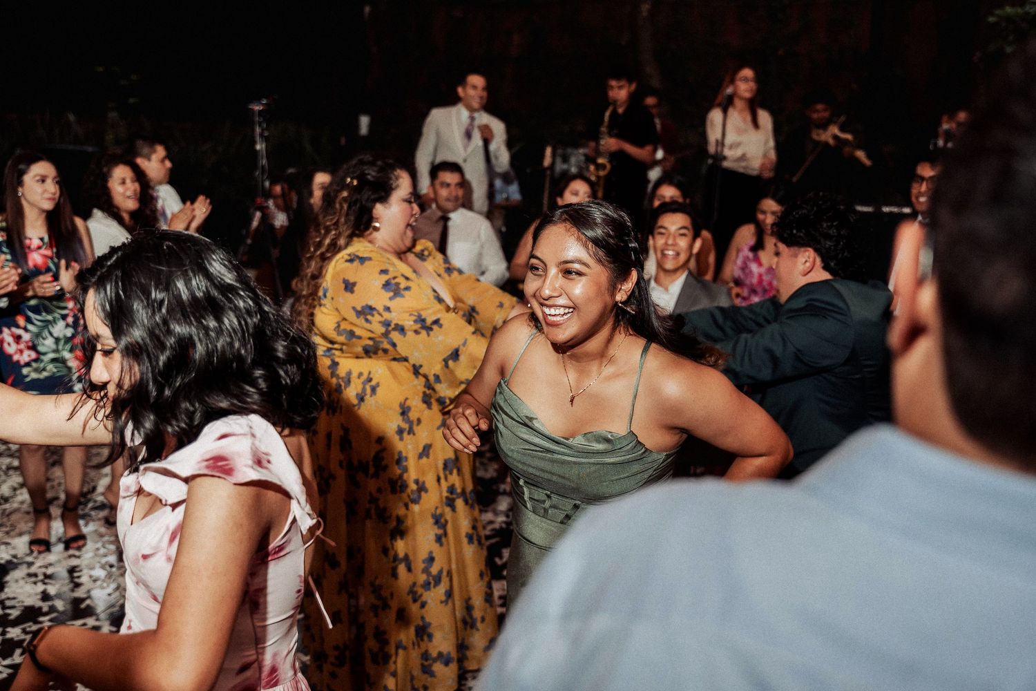 Wedding reception dance floor filled with guests celebrating and dancing in a dimly lit venue.