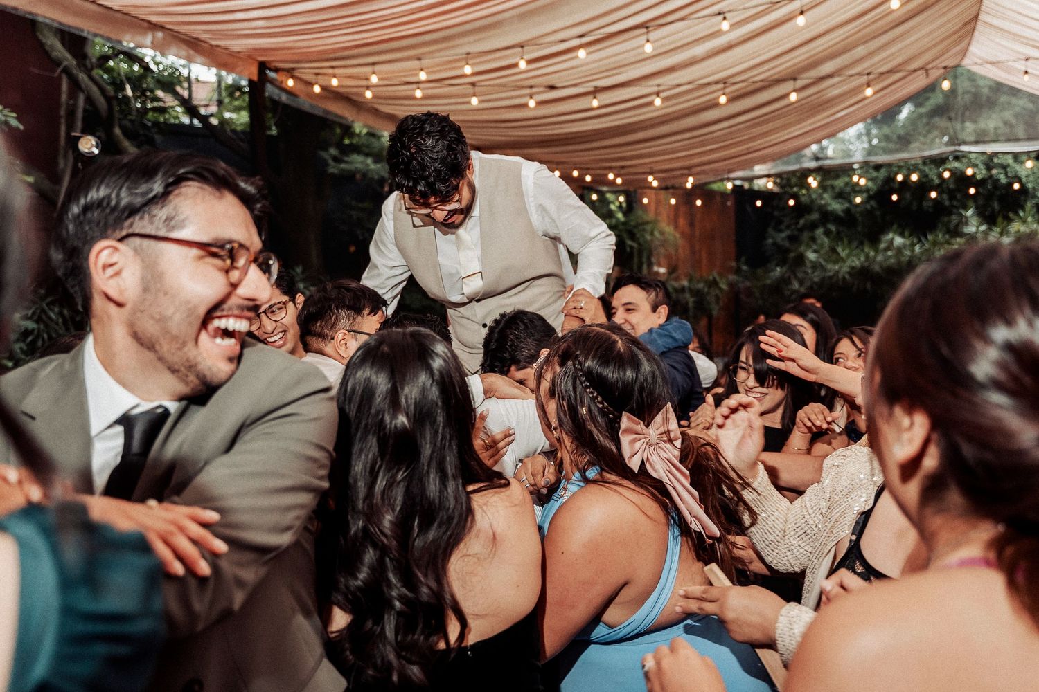Wedding reception celebration with guests dancing under draped fabric ceiling and string lights.