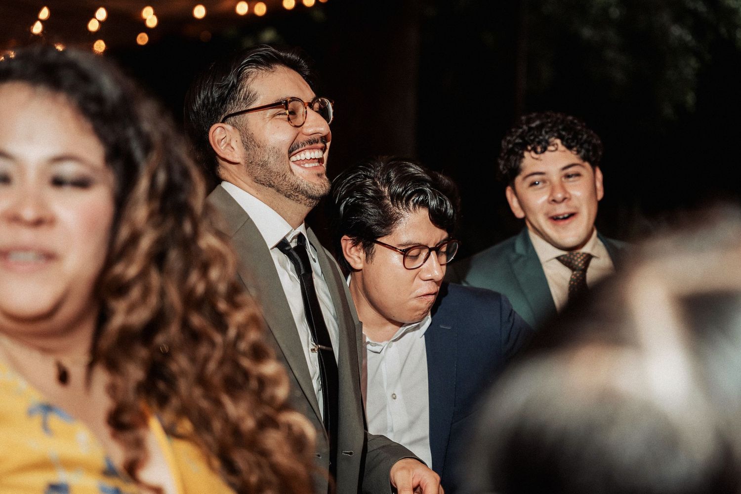 Candid reception moment showing joyful guests laughing under warm lighting.