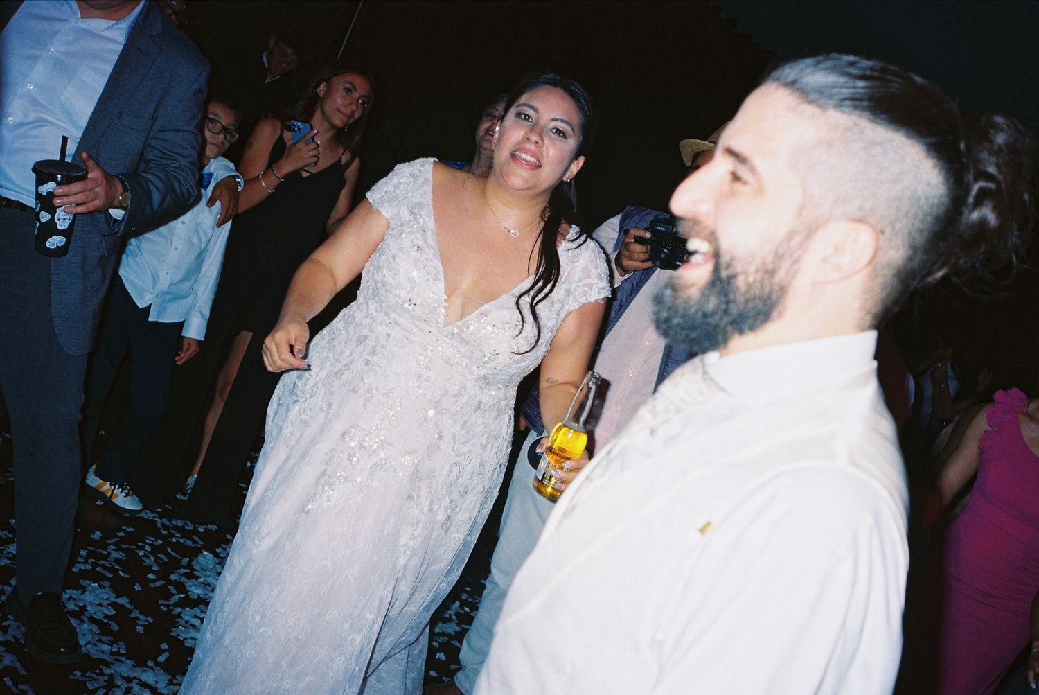 A group of people dancing and celebrating at a wedding reception on a dark dance floor.