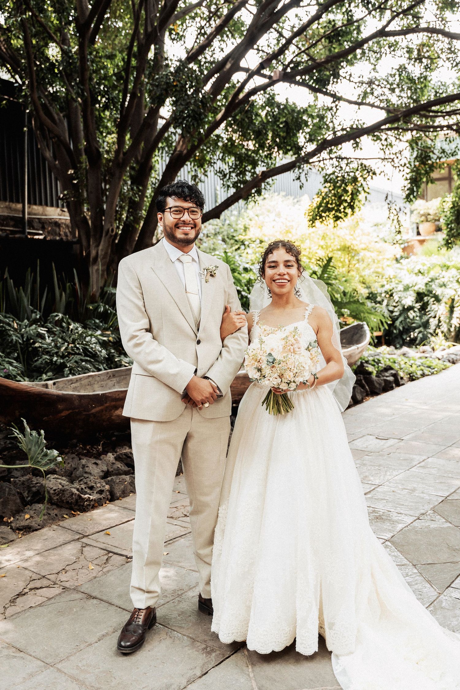 A newlywed couple in white and beige attire poses for romantic outdoor portraits along a stone pathway.
