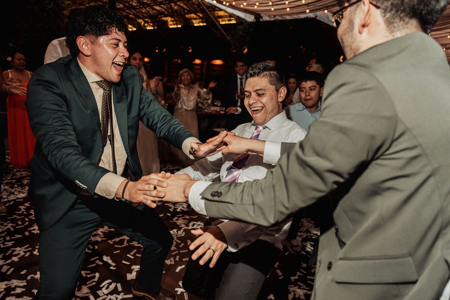 Wedding guests smiling and dancing together under dim lighting at an evening celebration.