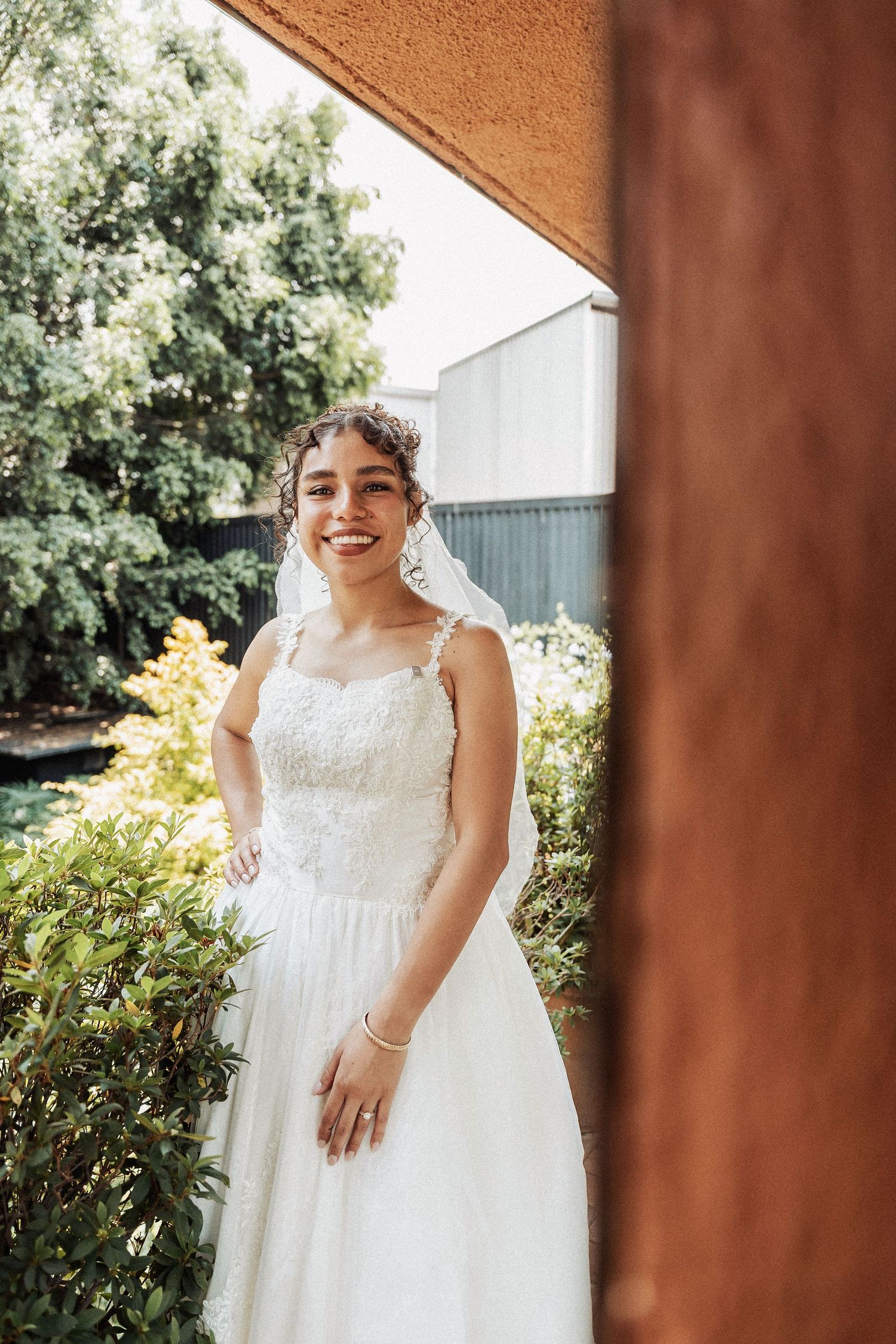 A person in a white lace wedding dress poses in a garden setting.
