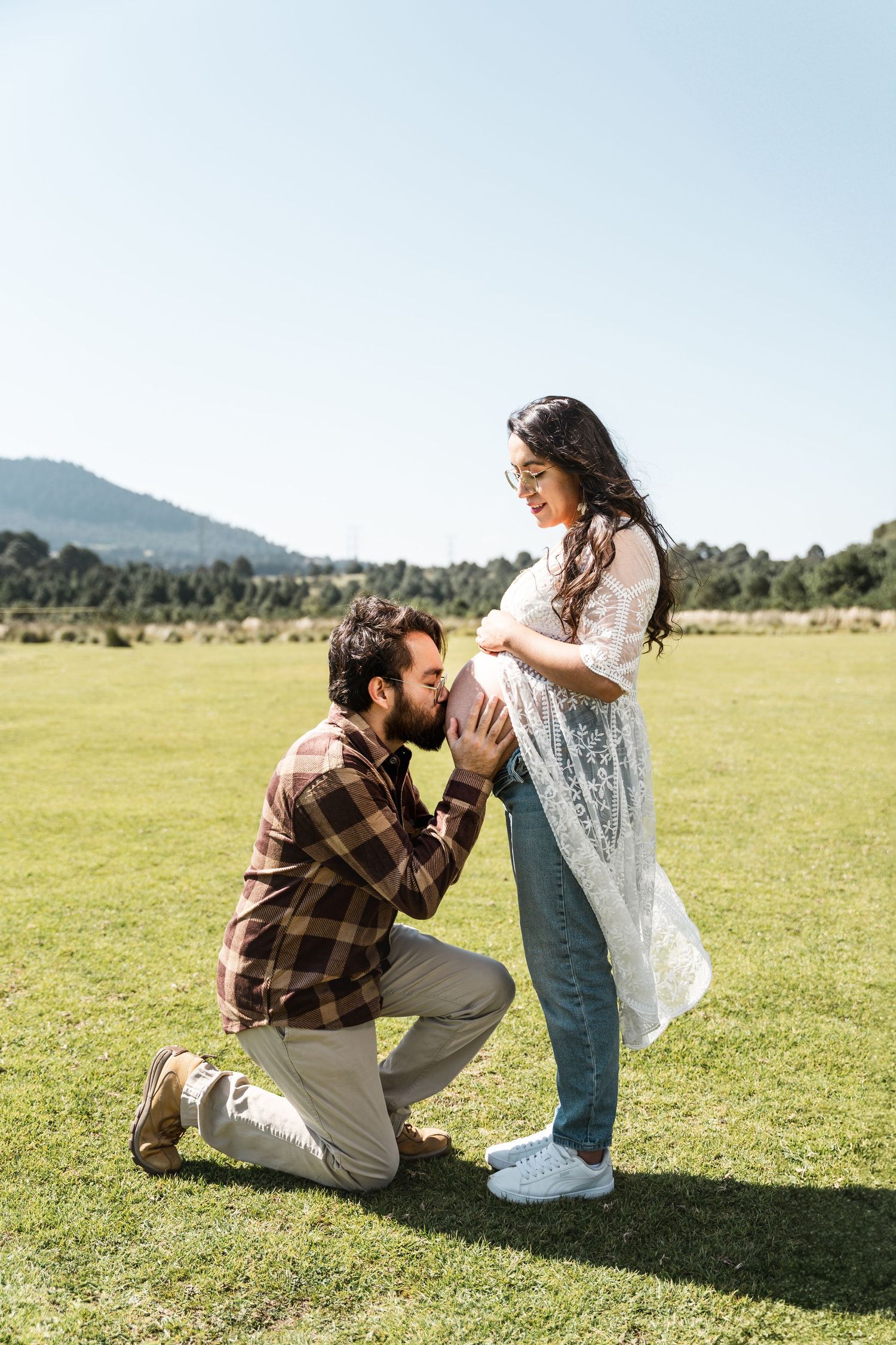 A romantic moment captured in a sunny meadow with mountains in the background.