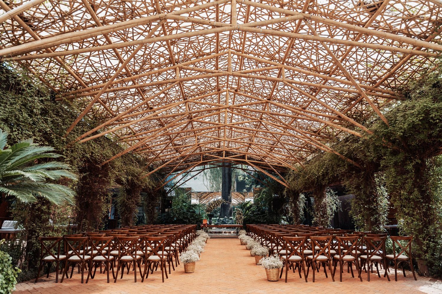 Rustic indoor wedding venue with wooden chairs beneath a stunning exposed beam ceiling and lush greenery decor.