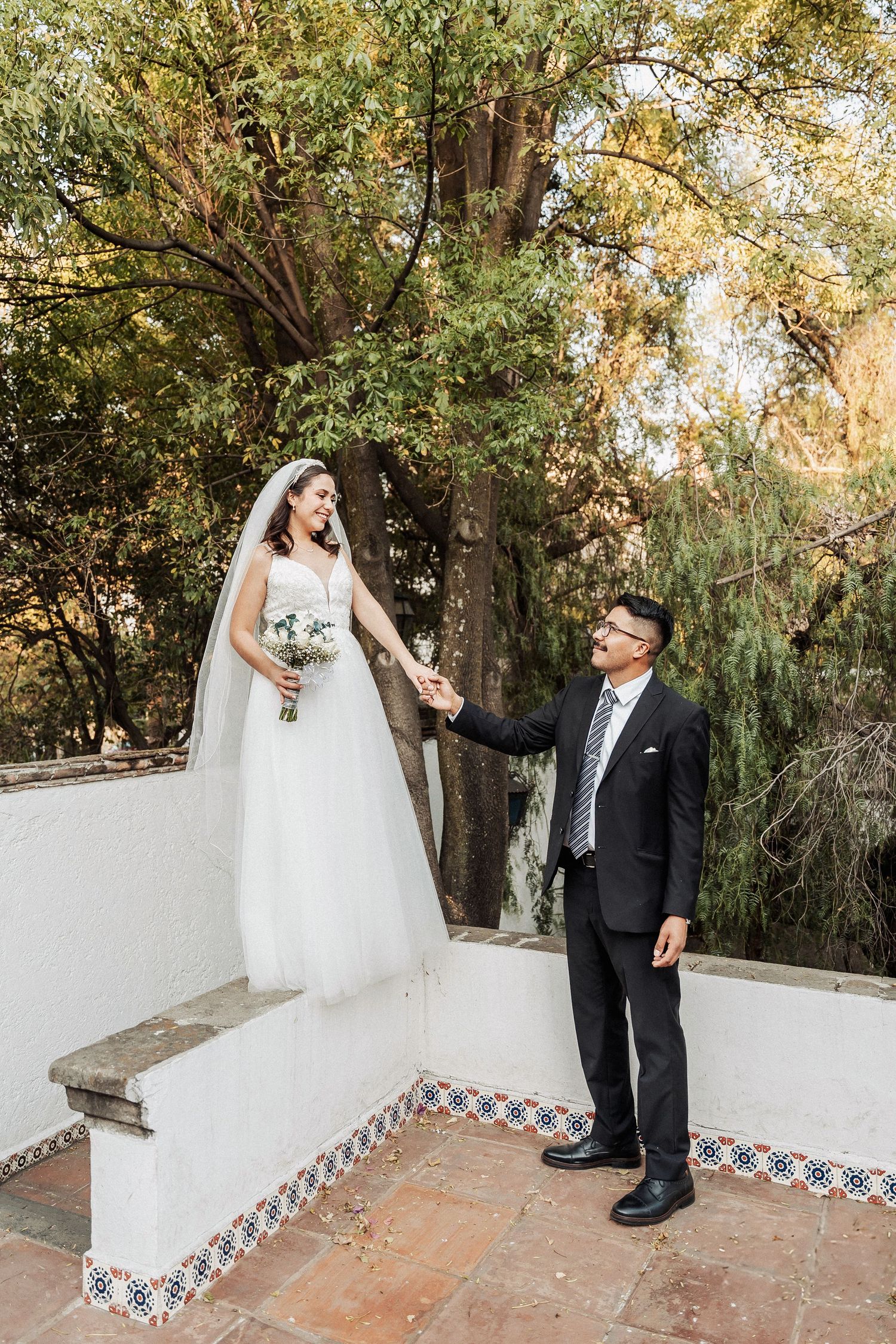 A couple shares a tender moment on decorative Spanish-style steps surrounded by lush greenery during their wedding day.