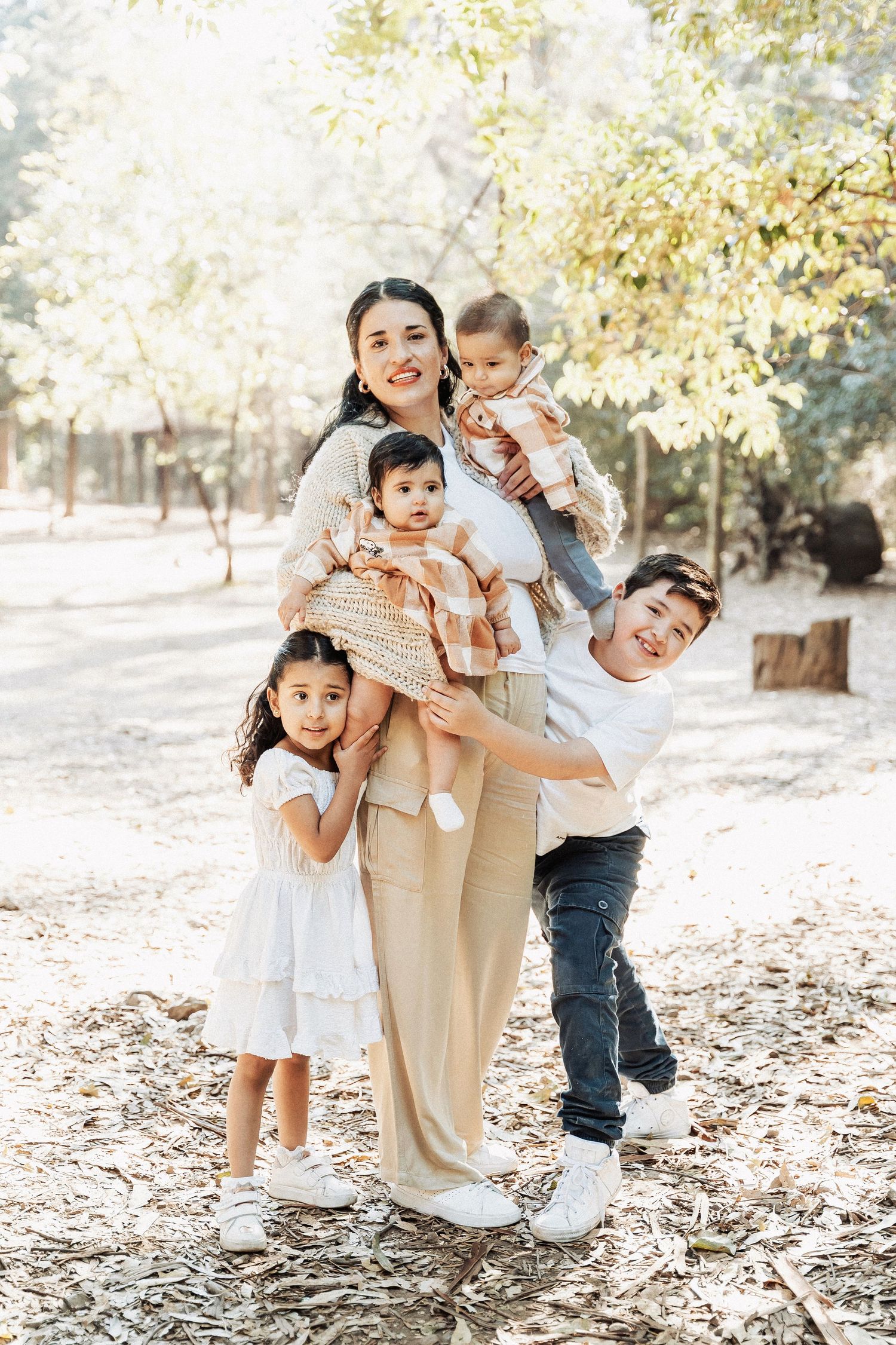 A family poses together outdoors on a sunny autumn day in casual attire among fallen leaves and trees.