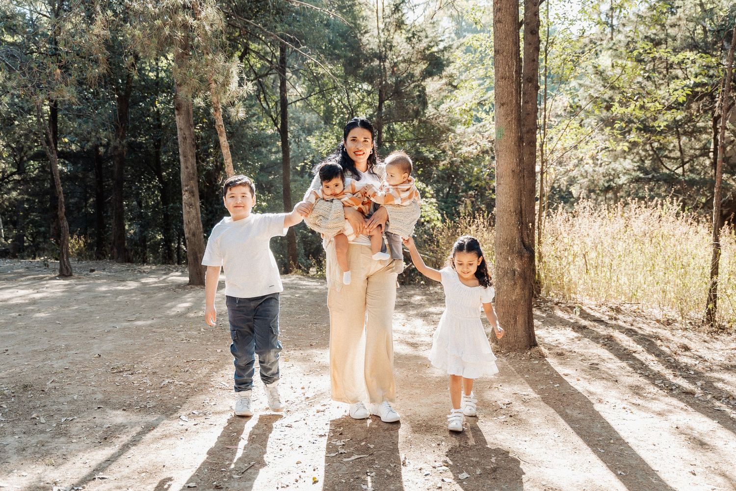 A family group enjoys a playful moment together in dappled sunlight on a forest path.