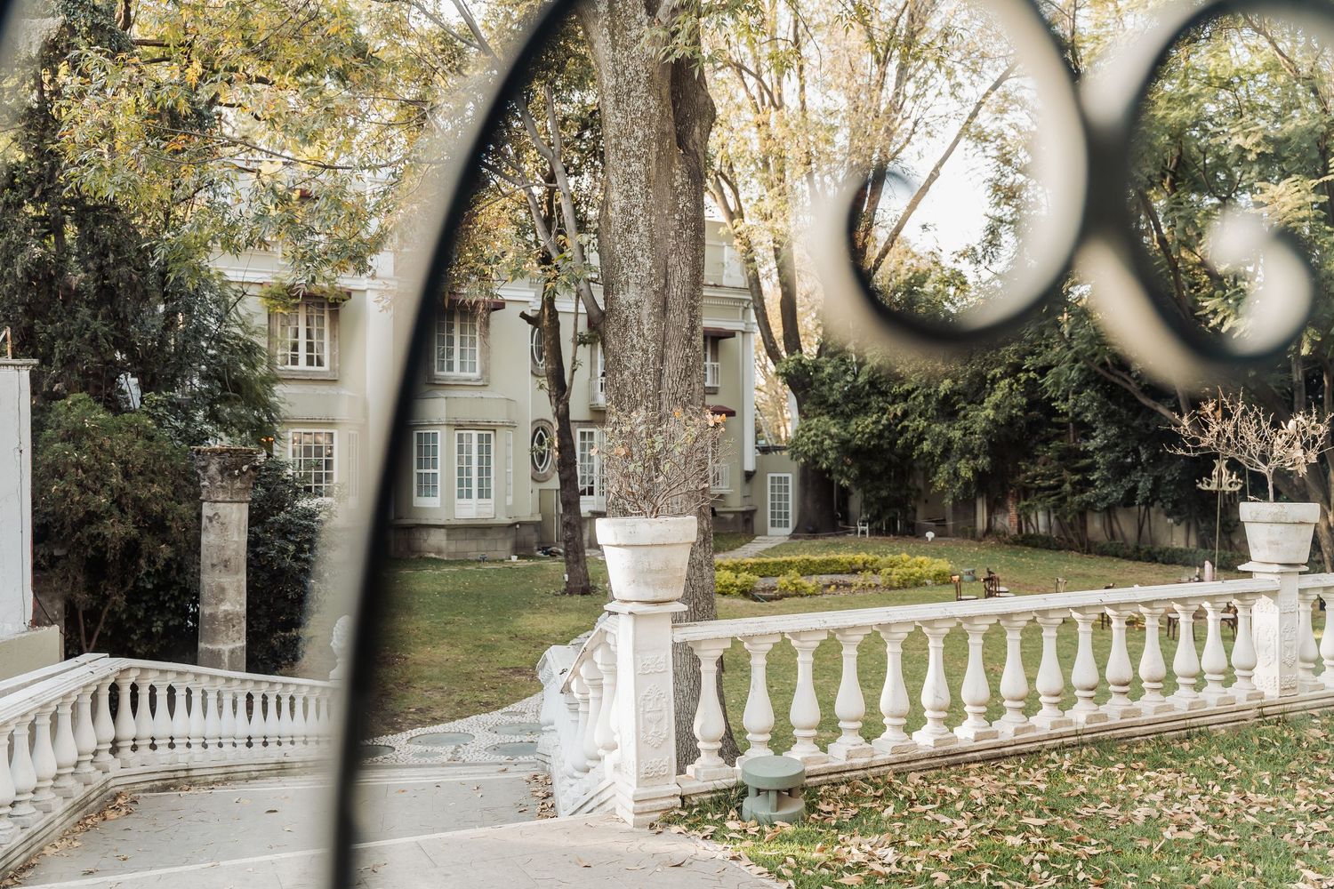 A decorative white stone balustrade railing in a garden park with autumn trees and an elegant building in the background.