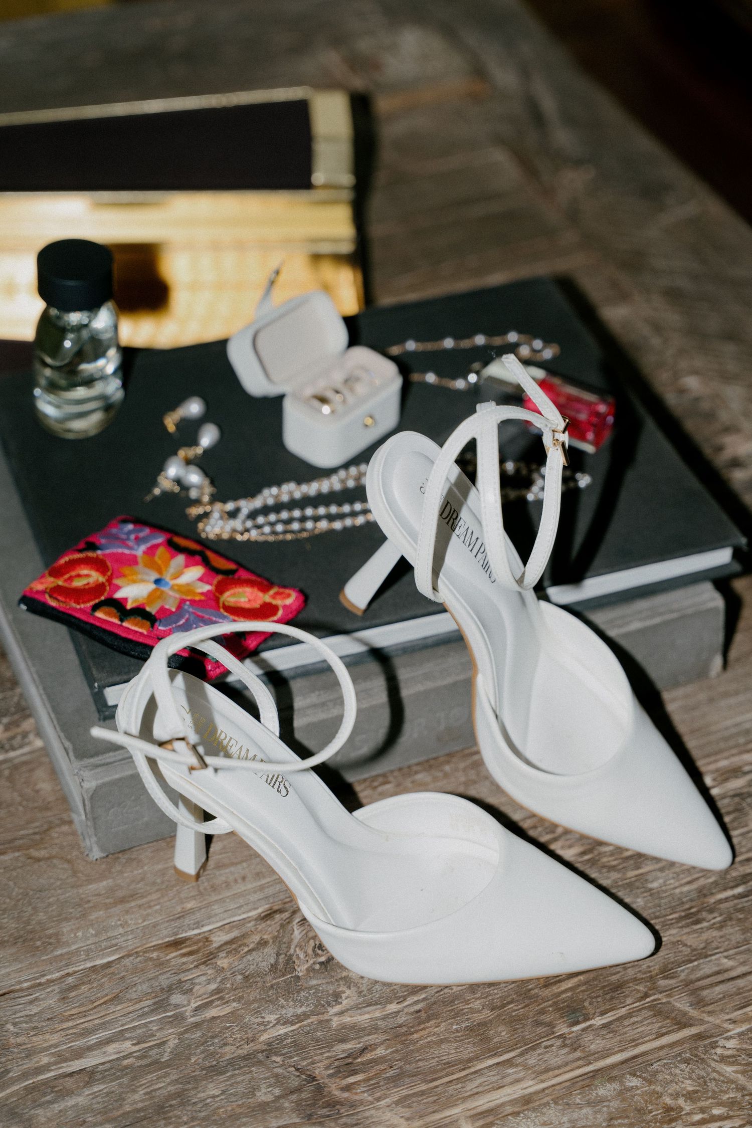 White bridal shoes displayed on a rustic wooden surface with jewelry and accessories in the background.