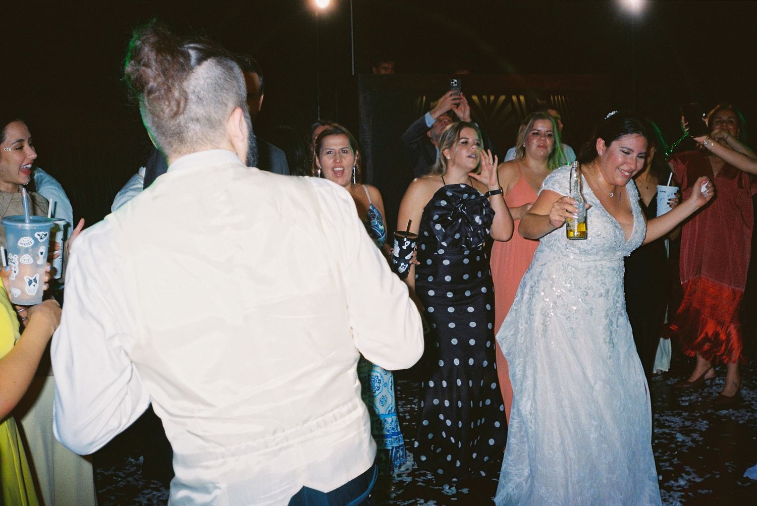 People dancing and socializing at a lively party or celebration event with dim lighting and festive atmosphere.