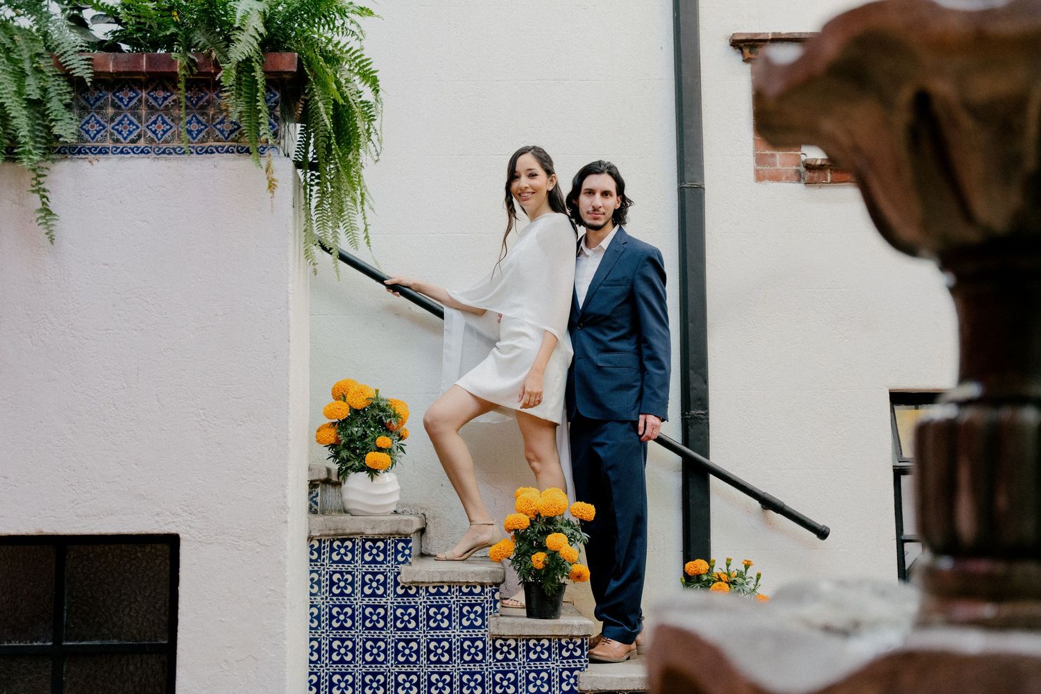 A couple poses together on outdoor stairs with yellow sunflowers and greenery in a romantic wedding setting.