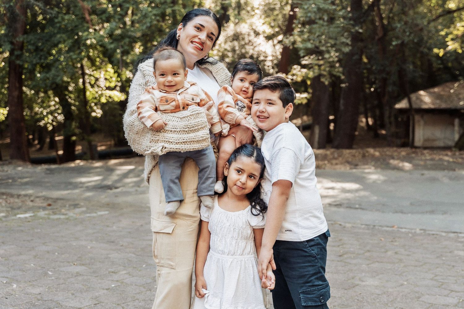A happy family poses together outdoors on a sunny day in a wooded park setting.