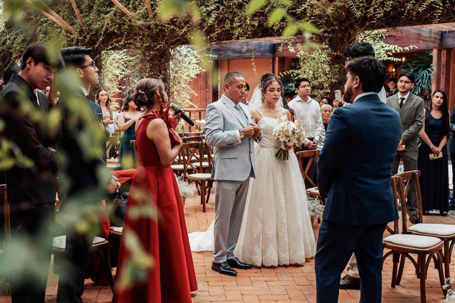 Wedding ceremony taking place in an outdoor garden setting with guests and natural greenery.