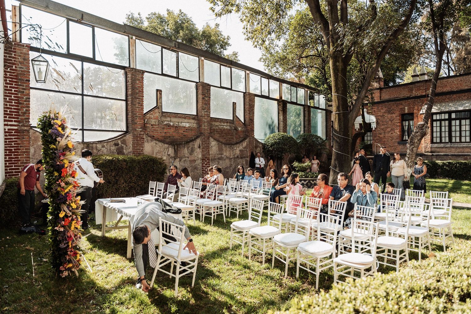 Outdoor wedding venue setup with white chairs and rustic decorations on a sunny day in front of a brick building.