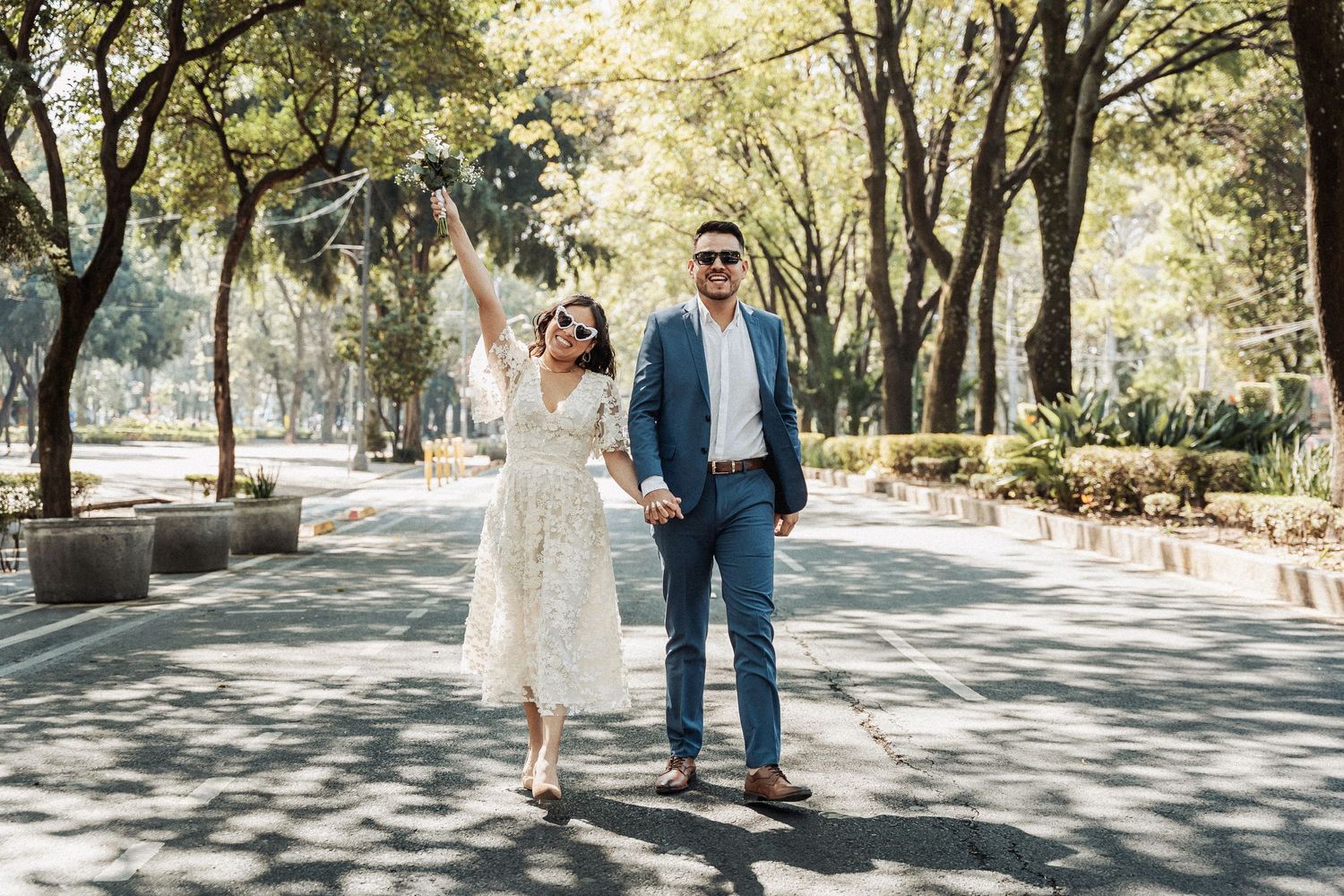 A couple celebrates while walking down a tree-lined pathway in formal attire.