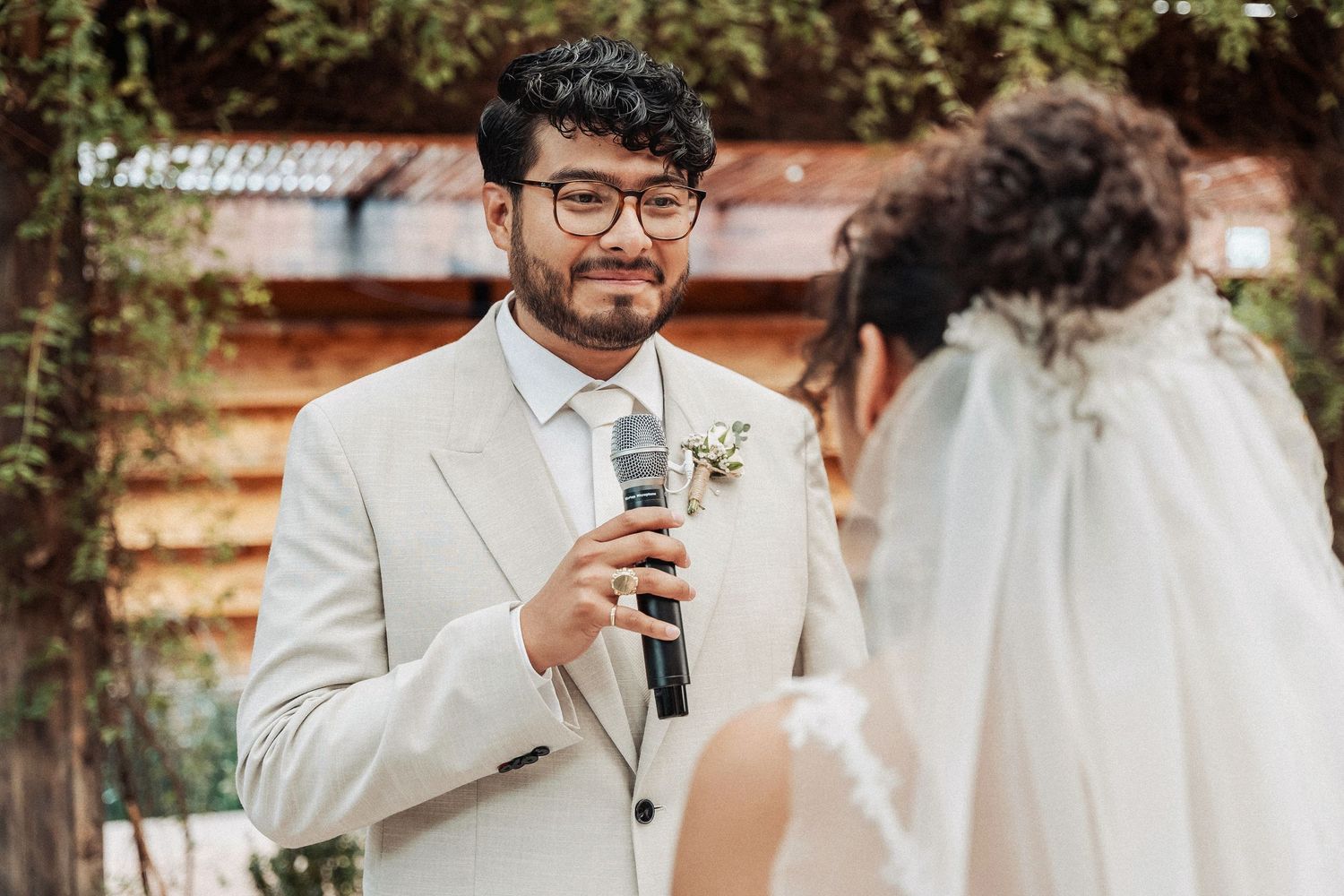 Wedding ceremony outdoors with speaker holding microphone in light colored suit.