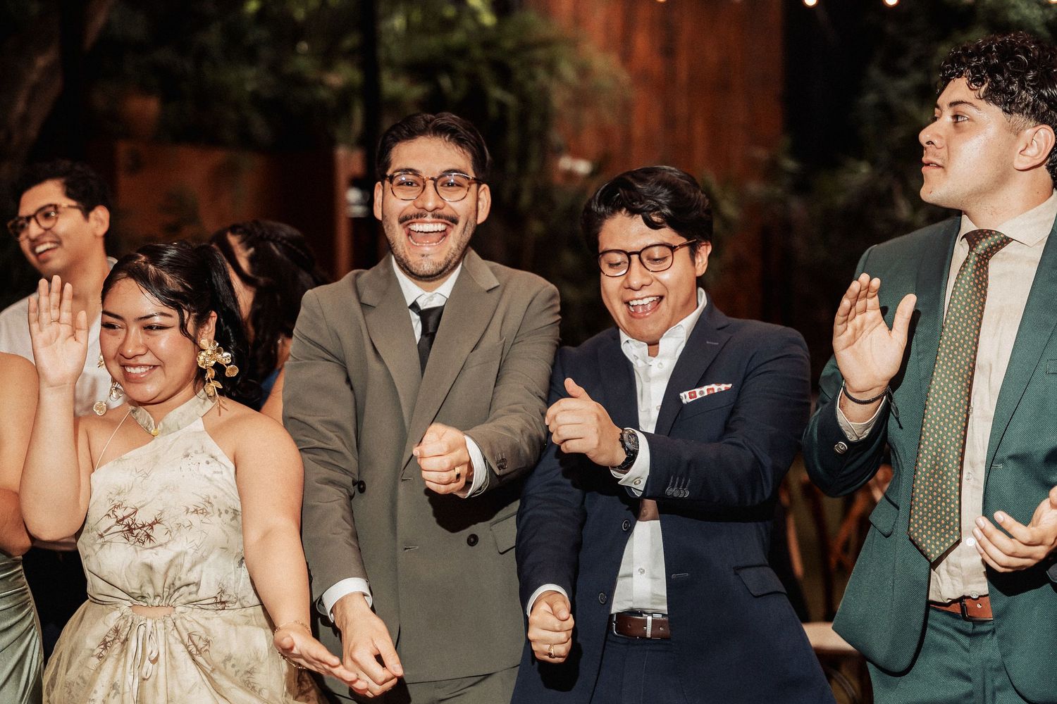 Wedding celebration scene with guests dancing and laughing together at an indoor venue.
