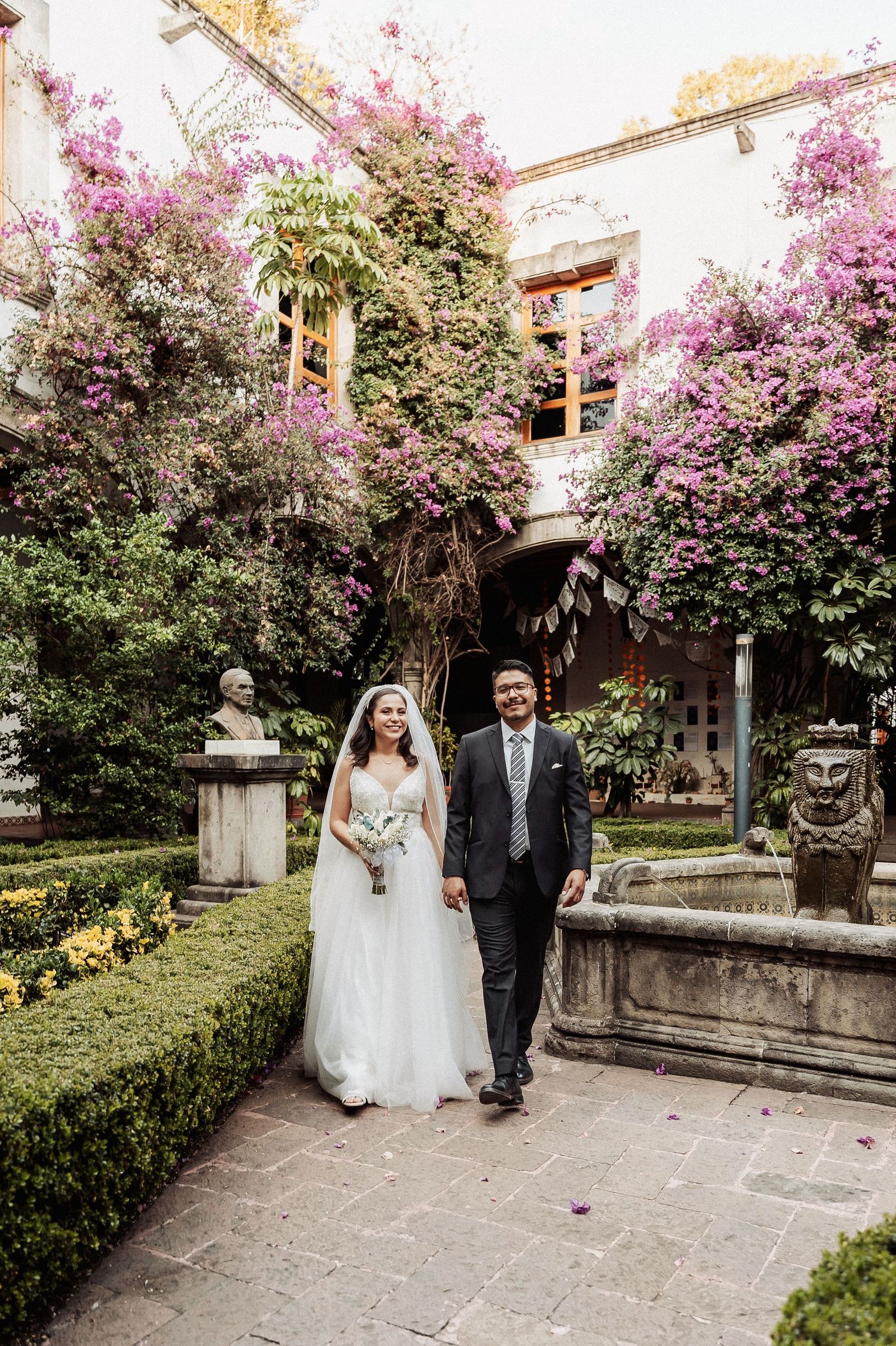 A wedding couple walking along a garden path surrounded by beautiful blooming purple crape myrtle trees.