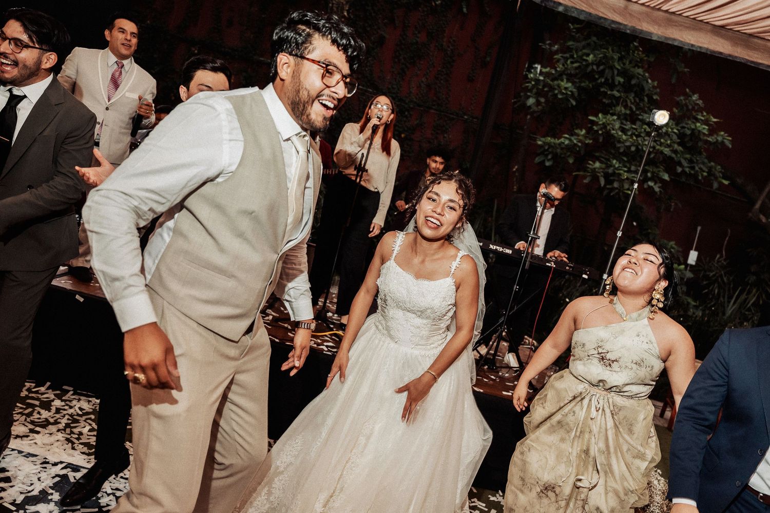People dancing and celebrating at a wedding reception with the bride in a white dress and guests in formal attire.