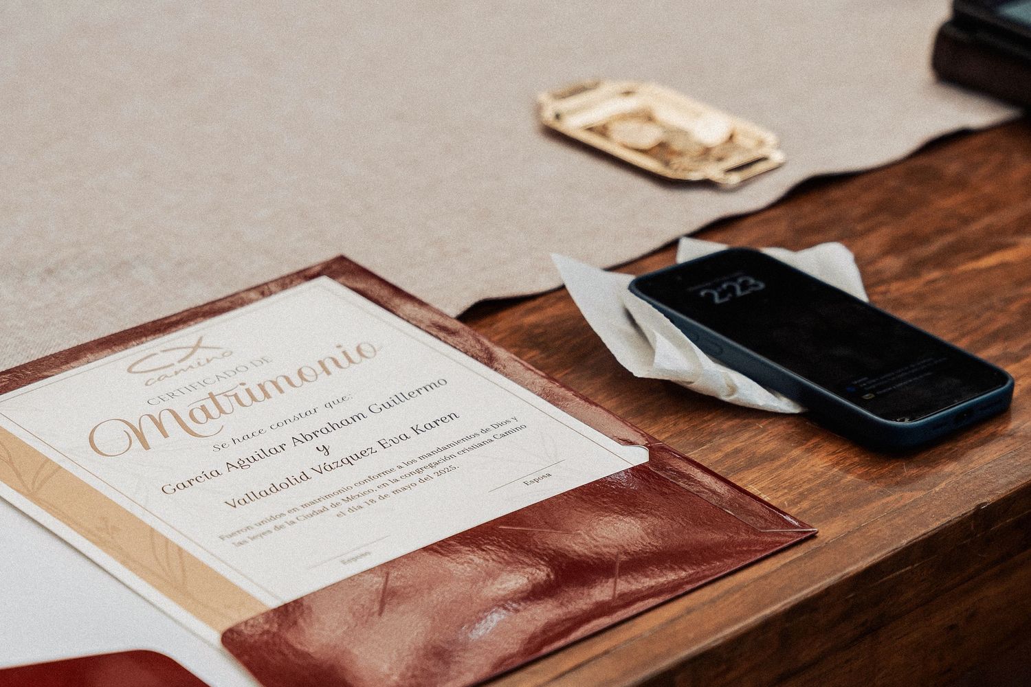 A ceremony program with elegant calligraphy lies beside a black smartphone and money on a wooden table.