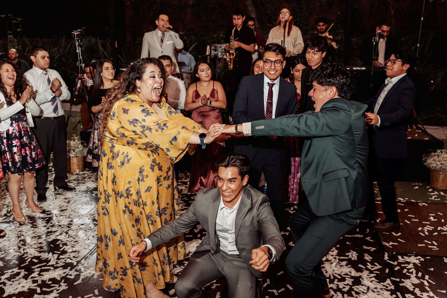 Lively wedding reception with guests dancing and celebrating on a confetti-covered dance floor.