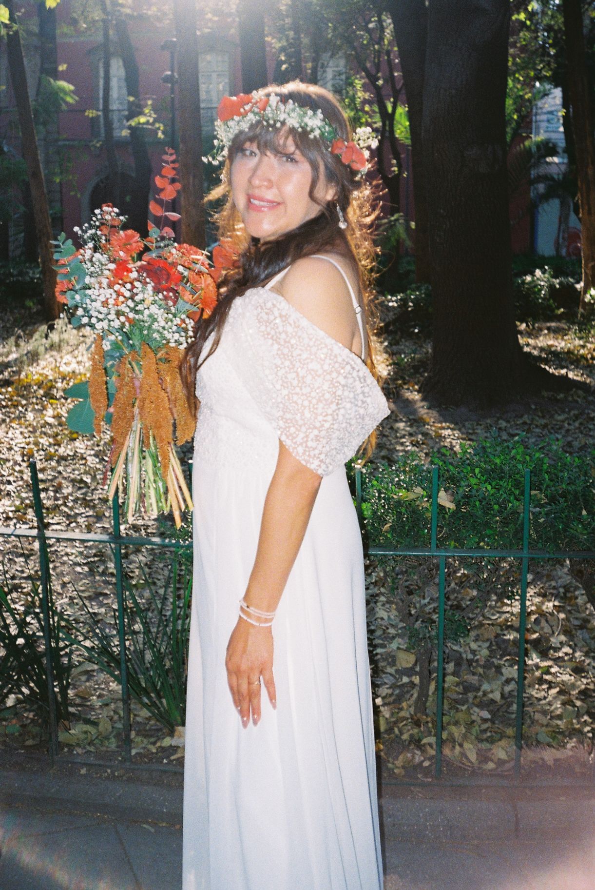 A person in a flowing white dress poses in a garden setting with decorative orange floral arrangements.