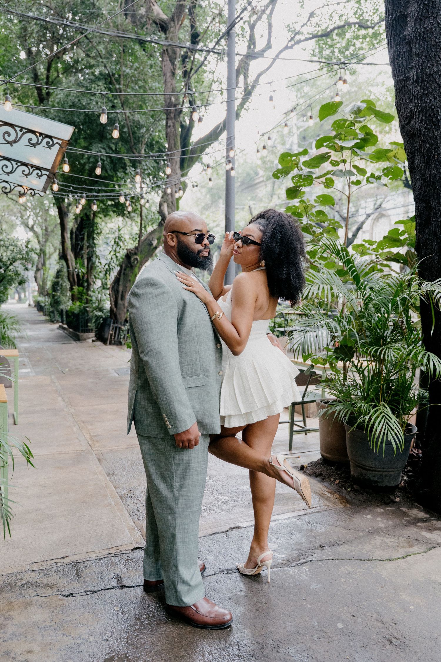 A couple in wedding attire shares romantic poses on a tree-lined path during their outdoor photo session.